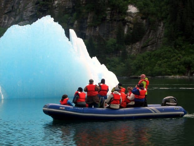 A group of people in a zodiac looking at a large piece of floating glacial ice in Alaska.