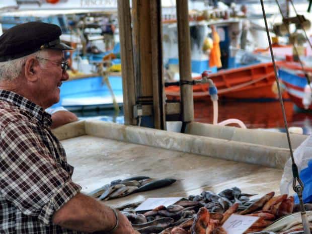 Local at the fish market with fishing boats in the background seen from a small ship excursion in Greece.