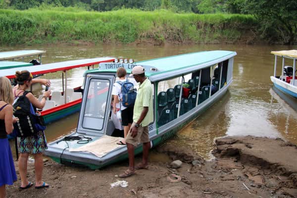 Families of travelers embarking on a covered open air boat on a river in Costa Rica.