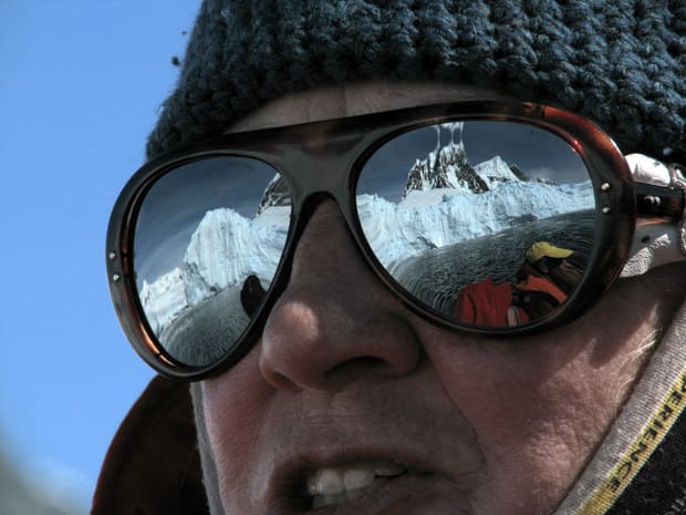 Close up of a small cruise ship crew member leading a skiff excursion in Antarctica wearing sunglasses reflecting the ice shelf and snowy peaks of Antarctica.