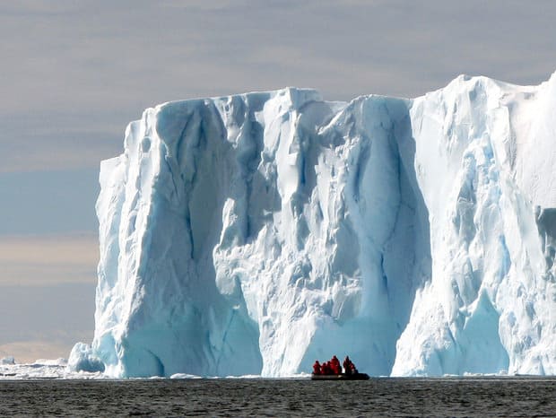 Guests aboard a small ship cruise in Antarctica on a skiff excursion up close to giant ice shelf.