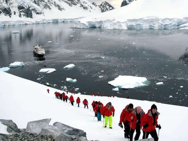 Group of guests on a hiking excursion on the snow in Antarctica with their small cruise ship in the background.