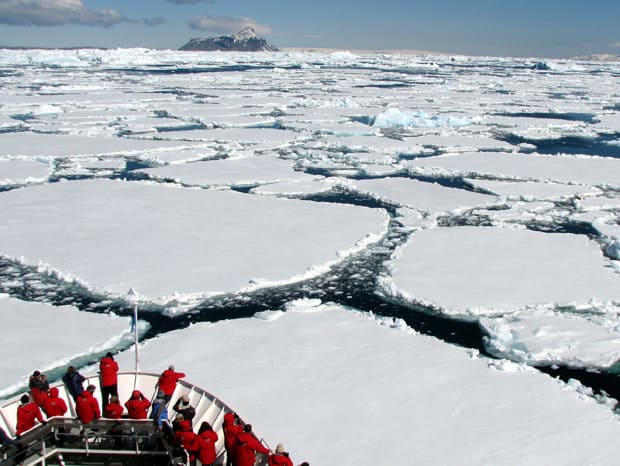 Guests on the bow of a small ship expedition cruise in Antarctica as the ship is breaking through the ice on the water.