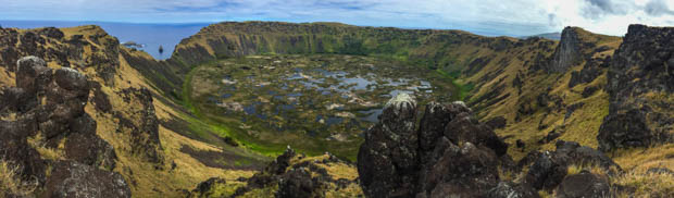 A crater hole with rocks, grass and ponds of water on the side of the ocean.