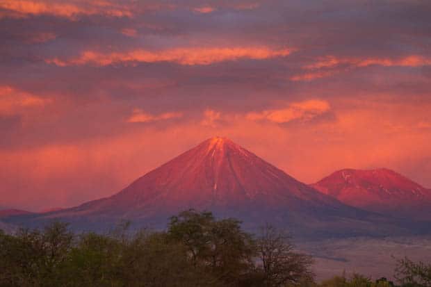 A volcano with the sun setting on the peak creating a pink sky and pink mountains in Atacama, Chile