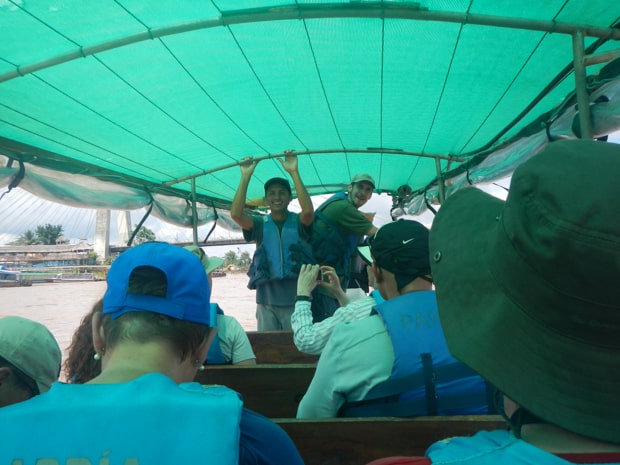 A group of travelers on a covered open boat motoring on the water.