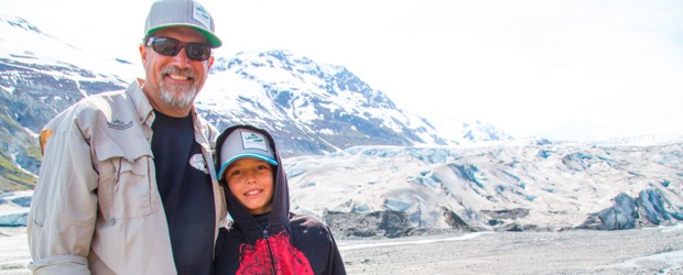 A father and son pose together in front of a glacier in Alaska