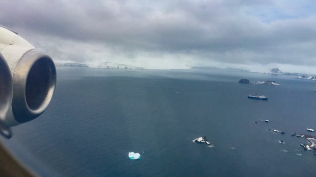 View from window seat with propeller of plane flying above icebergs while approaching Antarctica.