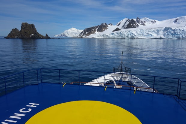 Bow of a small expedition cruise ship approaching land in Antarctica.