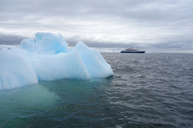 Small expedition ship cruising through Antarctica with iceberg in the foreground.