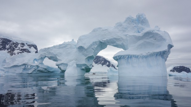 Unique arch shaped icebergs in Antarctica with a skiff in the distance seen from a small ship cruise.