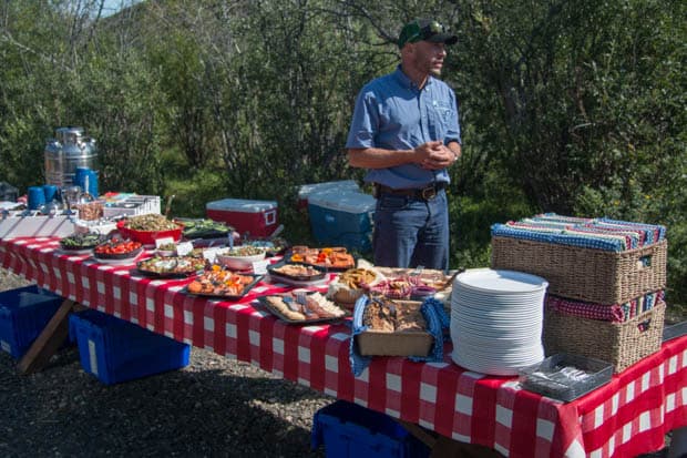 A man standing in front of a picnic table set with a lunch spread.