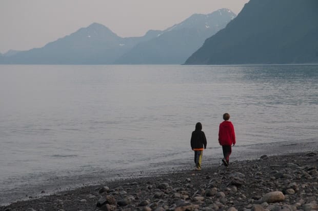 Two young boys walking along a beach in Alaska with mountains in the background.