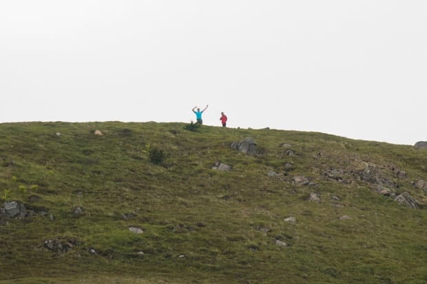 Two kids on a grassy knoll in Alaska posing with arms up in the air.