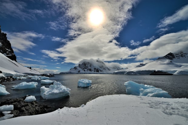 Sun behind clouds with mountains and icebergs in Antarctica.