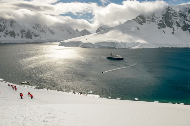 Guests hiking on snow with their small ship in the background in Antarctica.