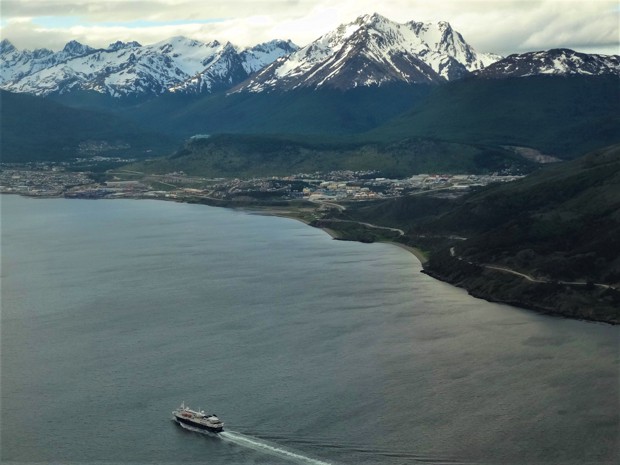 Small ship cruise seen from above departing the port of Ushuaia with the town and mountains in the distance.