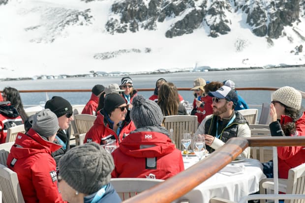 Guests aboard a small ship cruise in Antarctica enjoying the sun, food, and drink on the deck.