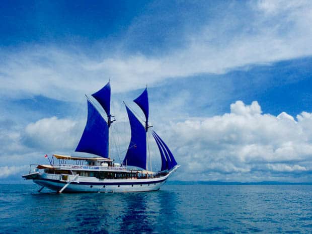 obak putih small ship cruising through the blue waters of Indonesia with her sails up.