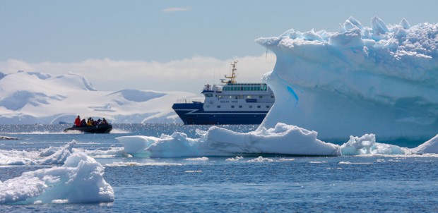 Small ship cruise in Antarctica behind icebergs with small skiff in front.