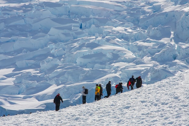 Guests from a small ship on a hiking excursion in Antarctica with only white snow formations in the background.