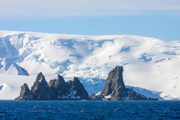 Landscape of jagged rocks and white hills in Antarctica seen from a small ship cruise.