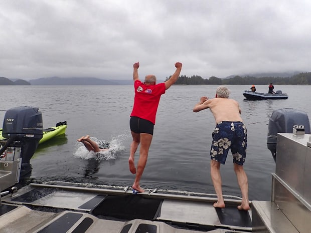 Guests aboard a small ship cruise in Alaska jumping into the cold water from the stern of the ship while doing a polar plunge.