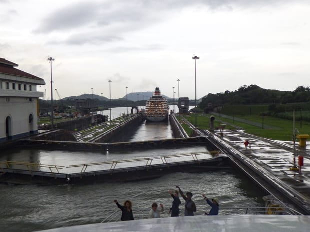People waving from the bow of a small ship cruise going through the locks in the Panama Canal.
