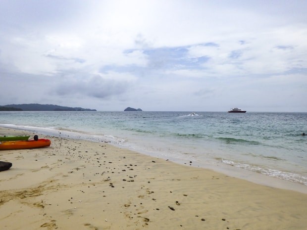 Kayaks resting on the beach at the pearl islands with a small ship in the background.