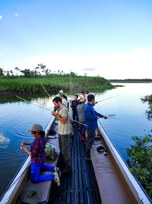 A group of people piranha fishing off a motorized canoe in the Peruvian Amazon jungle.