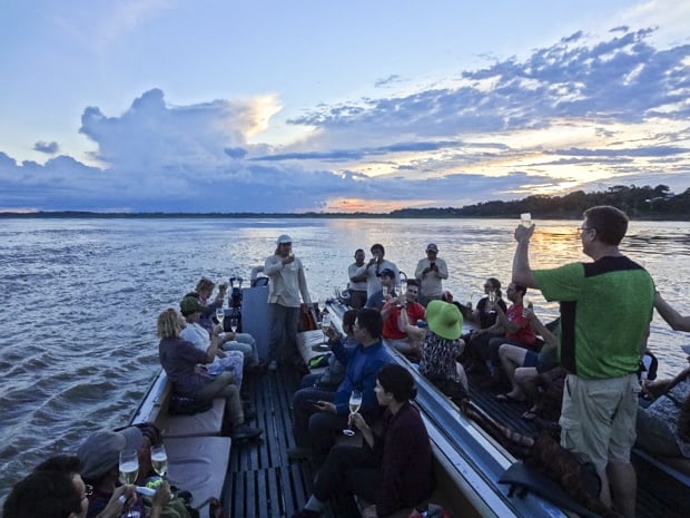 A group of people on a motorized canoe enjoying a champagne toast while the sun sets.