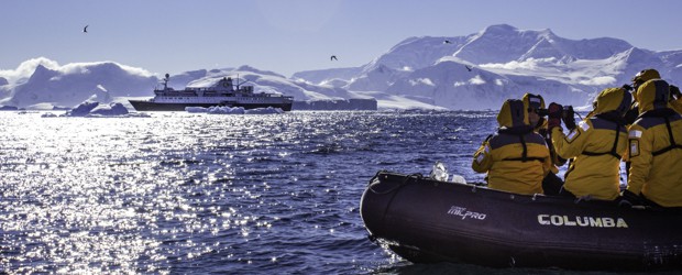 People on a skiff excursion taking a picture of their small cruise ship dwarfed by the snowy landscape of Antarctica.
