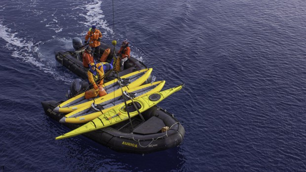 Kayaks being lowered from a small ship cruise in Antarctica and being prepared by the crew for the guests to use.