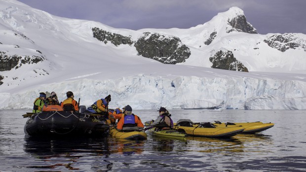 Small ship cruise guests entering kayaks from skiff in Antarctic.