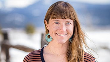 Travel expert Lis Larson portrait with blue earrings and a striped brown shirt