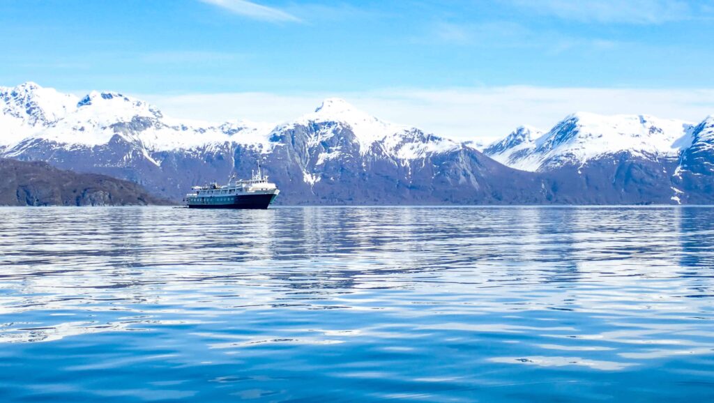 A reflection on the blue water of the snow capped mountain range and the alaska small ship -wilderness adventurer floating on the horizon