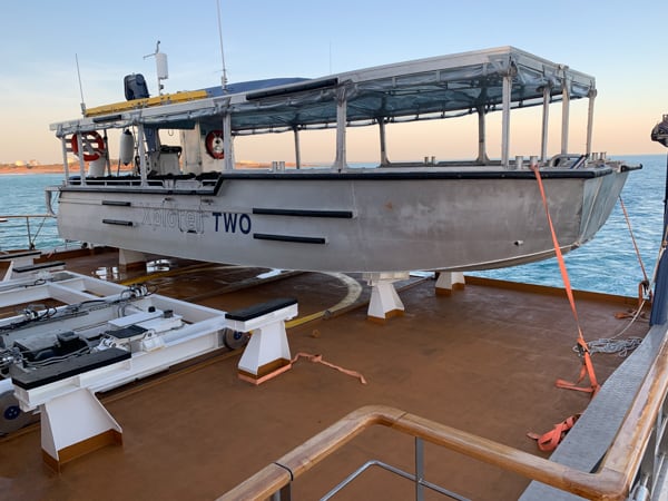 A small expedition vessel called Explorer Tender docked on the Coral adventurer, a white open air boat with seats