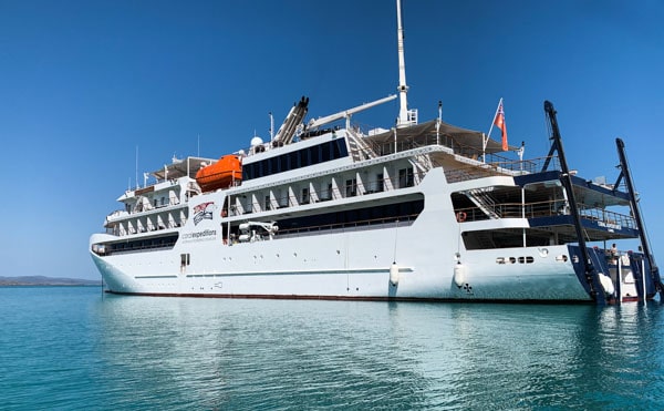 Australia small ship Coral Adventurer floats in the teal ocean against bright blue cloudless sky