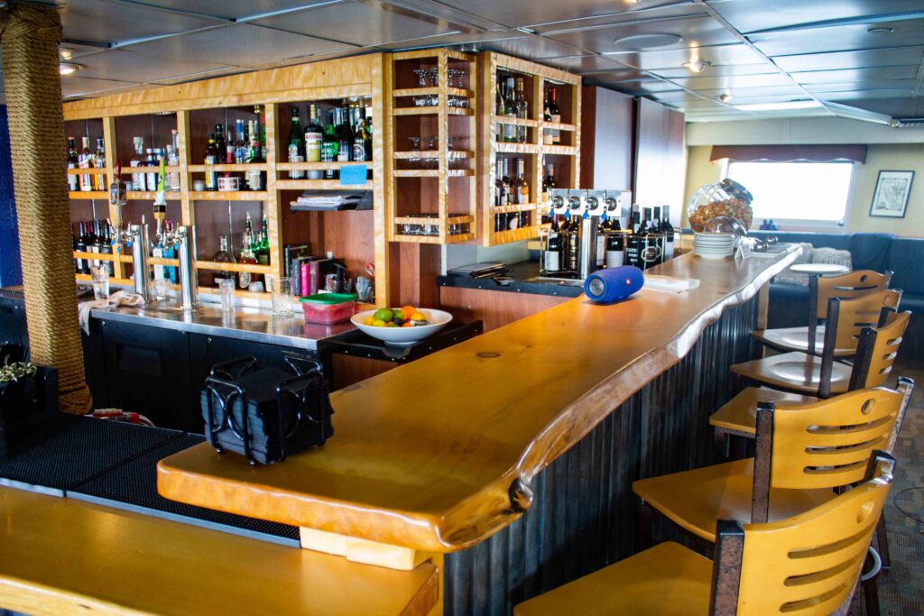 a photo of the bar aboard Wilderness Adventurer, showing glossy wooden counter tops with, wooden high chairs, cubbyholes are full of spirits, alcohol and other beverage choices