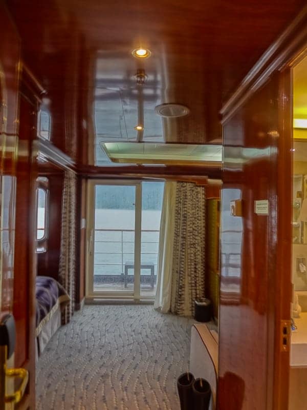 a rich wooden suite cabin aboard hebridean sky polar expedition ship shows the end of the bed and a sliding glass door out to a private balcony.