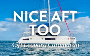 White Belize catamaran Nice Aft Too with blue sail storage jacket & lots of windows sits in calm water on a sunny day.
