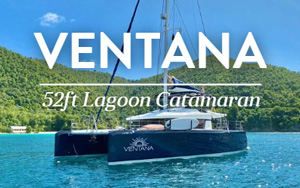 Belize catamaran Ventana al Mar with dark blue hulls & white upper deck sits in turquoise water in sun by bright green island