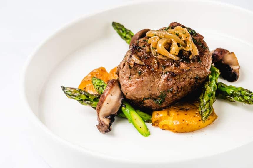 a dinner plate of steak, asparagus, potatoes, mushrooms and caramelized onions, served aboard luxury galapagos yacht, origin, theory and evolve.