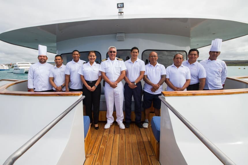 the captain and crew stand in white and navy blue aboard luxury Galapagos yacht origin, theory and evolve, all available for chartering