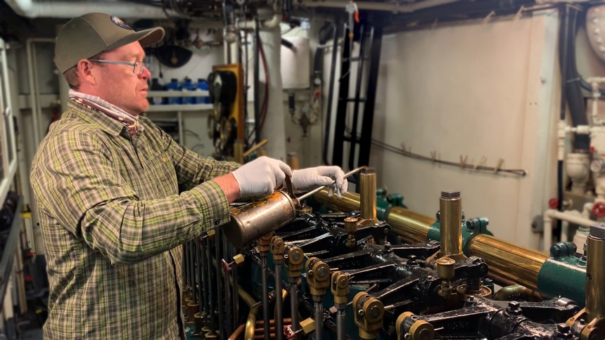 Wearing white gloves Catalyst engineer oils the historic 1932 diesel engine around each piston
