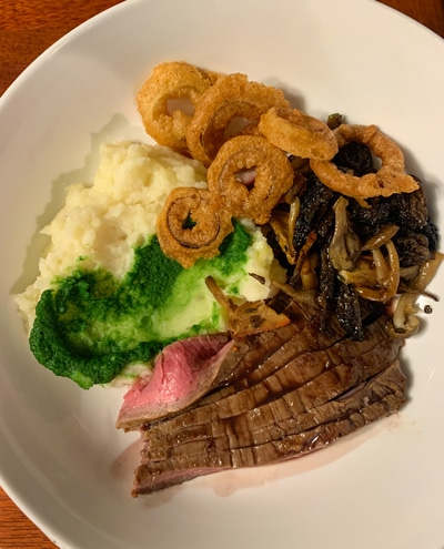 A dinner plate served aboard Alaska small ship catalyst, mashed potatoes, fried onions and steak on a white plate.