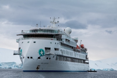 Exterior view of the modern Antarctic expedition ship Greg Mortimer, white and futuristic looking as it cruises the ocean.