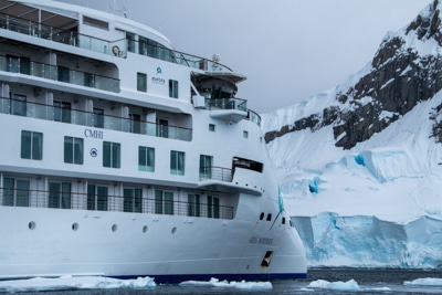 The front exterior of modern Greg Mortimer ship, futuristic and white with decks of windows and wrap around walkways.