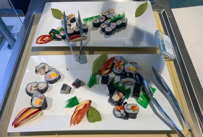 Two white serving plates filled with colorful sushi rolls and metals tongs, part of buffet dinner aboard Greg Mortimer ship.