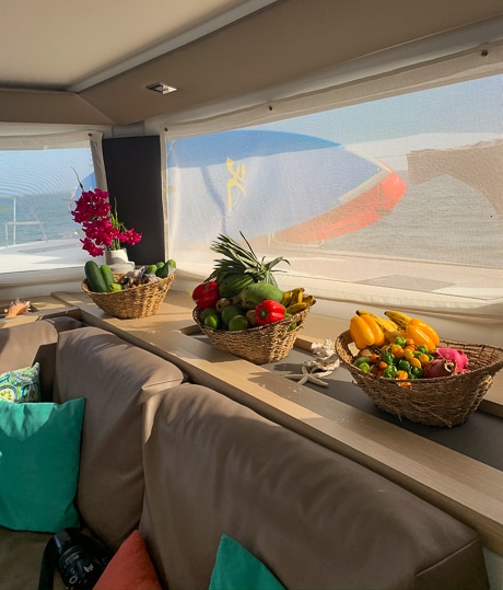 Aboard a Belize charter catamaran three baskets of brightly colored fresh fruit and vegetables sit on the window sill inside.